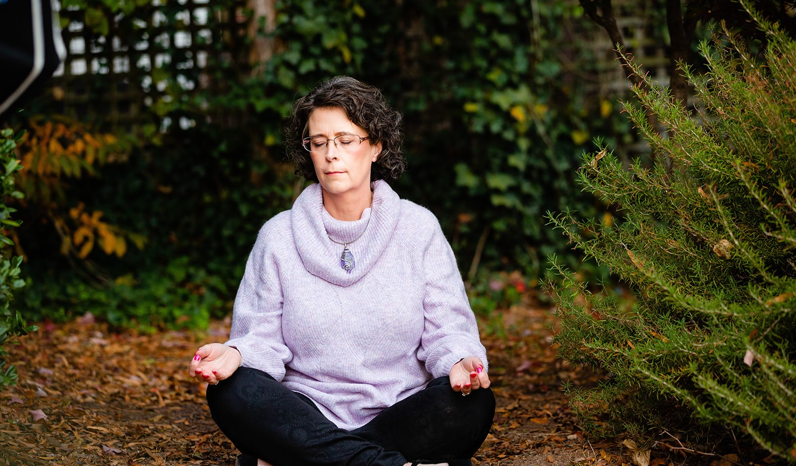 Hilarie Cox in Meditation Hilarie Cox meditating outdoors surrounded by trees and greenery.